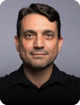 Professional headshot of a man wearing a black shirt against a neutral gray background.